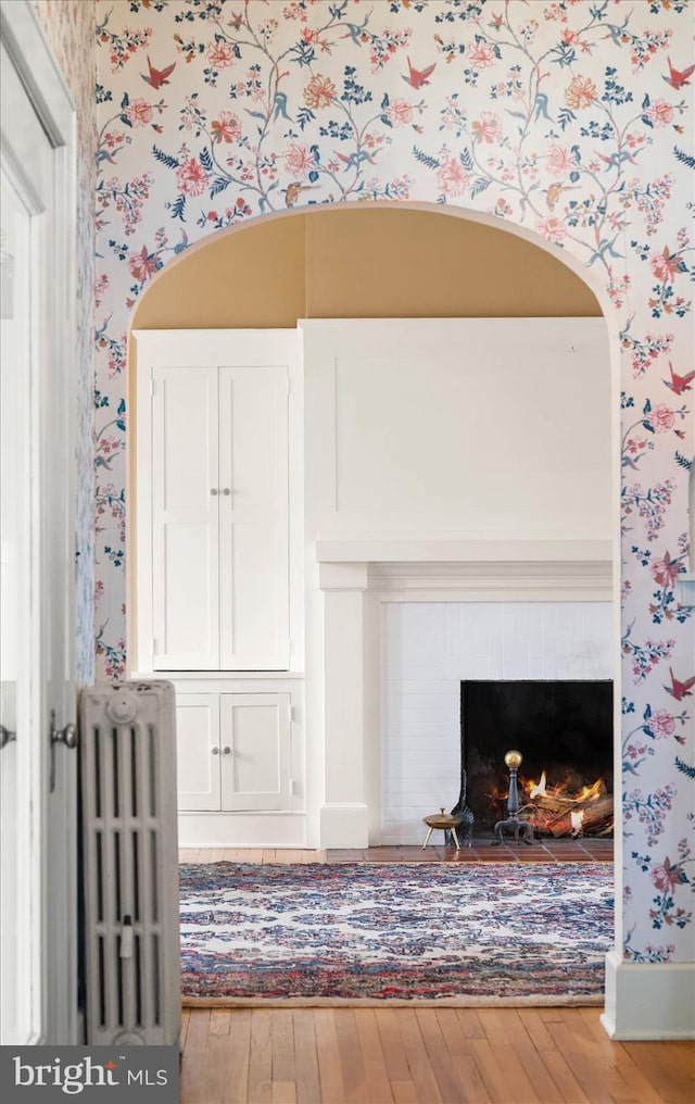 room details with radiator, a brick fireplace, wood finished floors, and wallpapered walls