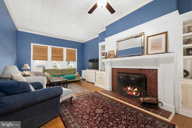 living room with a brick fireplace, built in shelves, crown molding, and wood finished floors