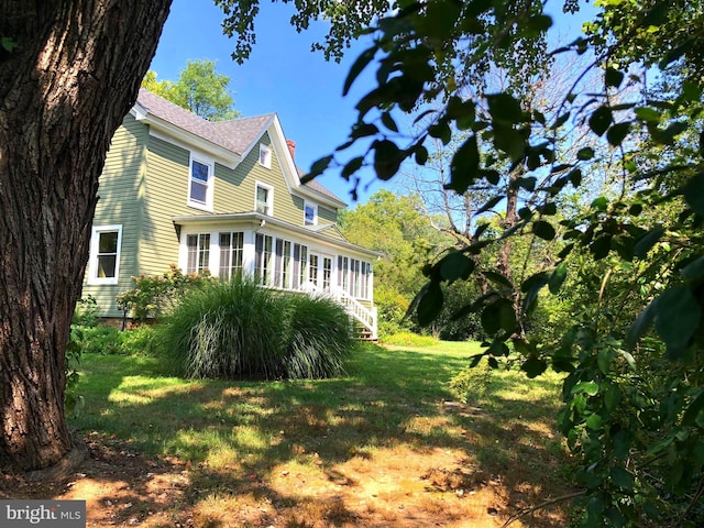 view of property exterior featuring stairs, a lawn, a chimney, and a sunroom