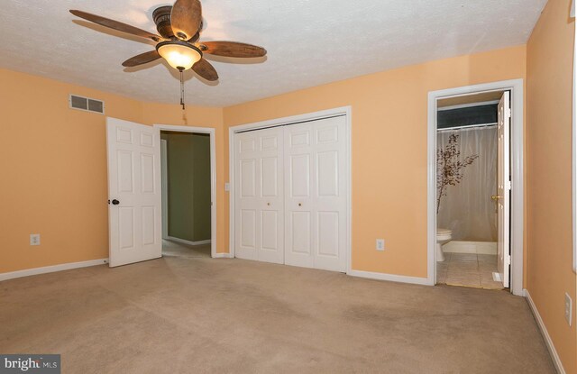 unfurnished bedroom with ensuite bath, a closet, a textured ceiling, light carpet, and ceiling fan