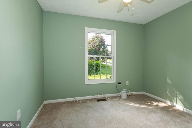 carpeted spare room featuring a textured ceiling, ceiling fan, and a healthy amount of sunlight