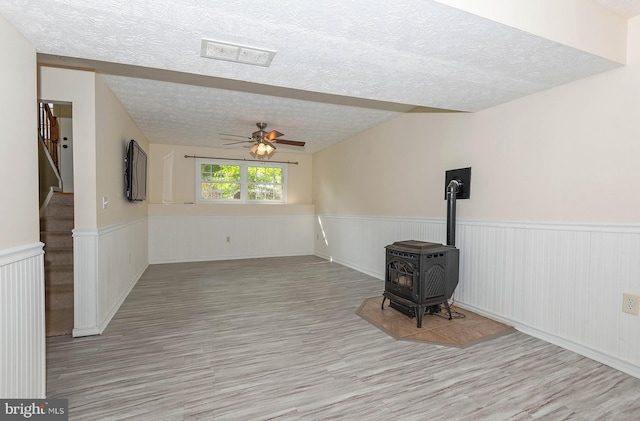 living room with ceiling fan, a wood stove, and a textured ceiling