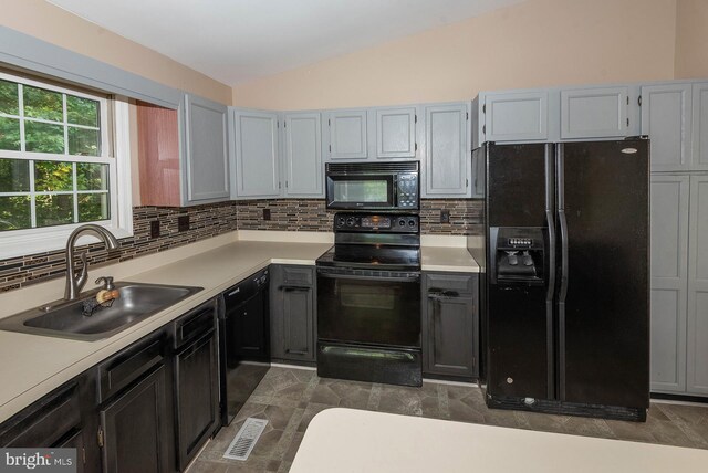 kitchen with tasteful backsplash, vaulted ceiling, sink, dark tile patterned flooring, and black appliances