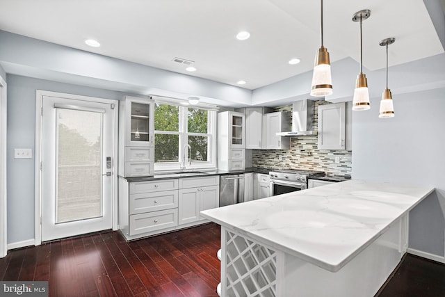 kitchen featuring pendant lighting, stainless steel appliances, dark hardwood / wood-style flooring, kitchen peninsula, and wall chimney exhaust hood