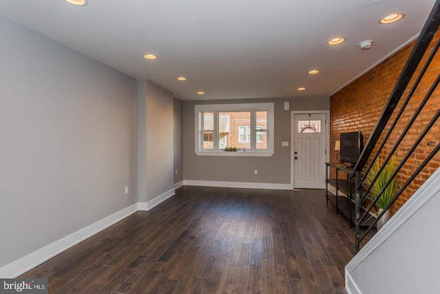 unfurnished living room with dark wood-style floors, brick wall, recessed lighting, and baseboards