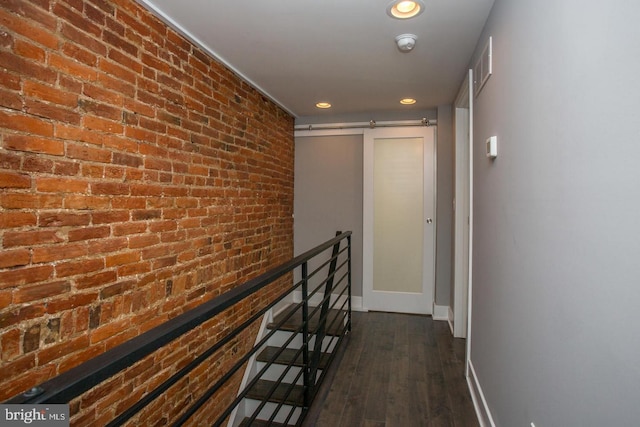 hall featuring brick wall, dark wood-type flooring, and a barn door