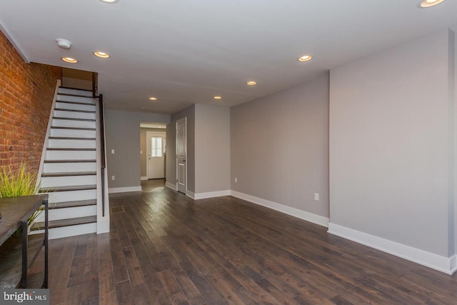 spare room featuring dark hardwood / wood-style flooring and brick wall