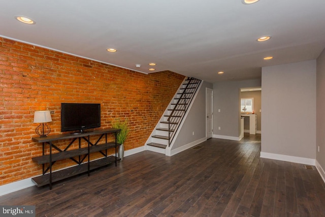 living area featuring dark wood-style floors, baseboards, stairway, and brick wall