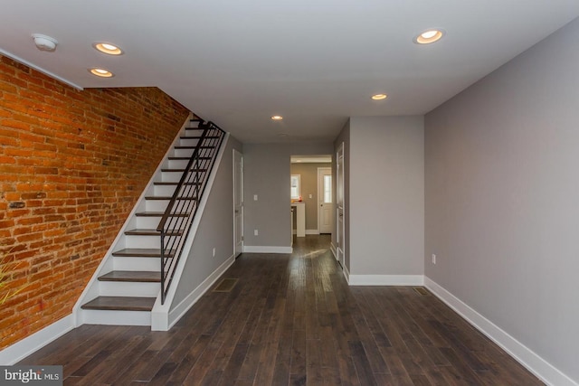 interior space featuring dark wood-style floors, baseboards, and brick wall