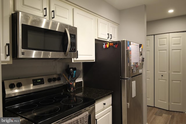 kitchen featuring hardwood / wood-style floors, stainless steel appliances, dark stone counters, and white cabinets