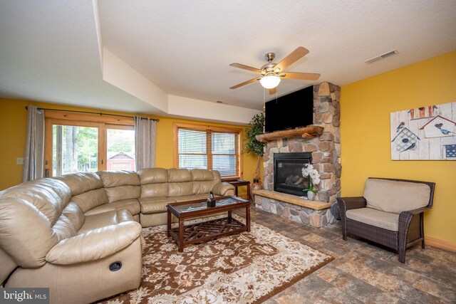 living room featuring ceiling fan and a stone fireplace