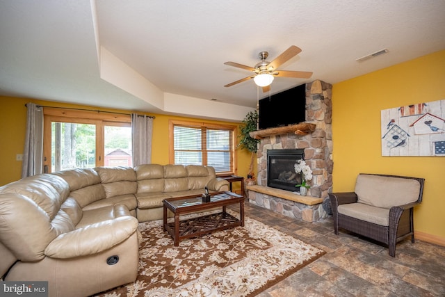 living room featuring ceiling fan, a fireplace, visible vents, baseboards, and stone finish flooring