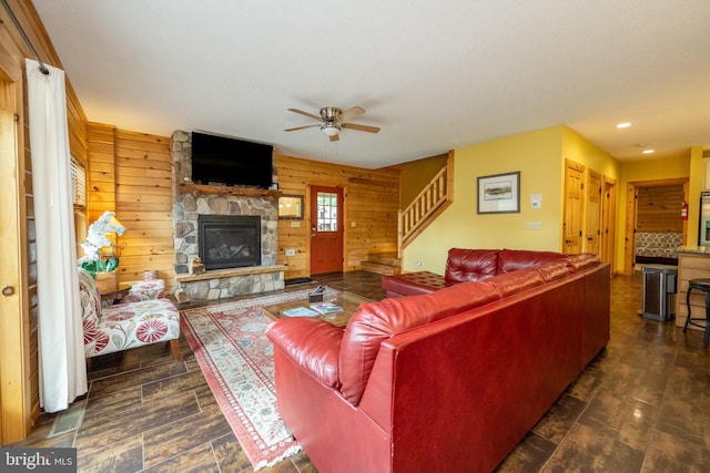 living room featuring wooden walls, ceiling fan, and a stone fireplace