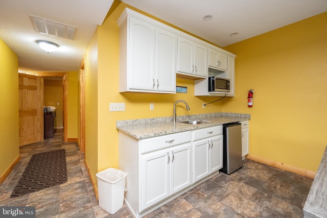 kitchen featuring light stone counters, stainless steel appliances, sink, and white cabinetry