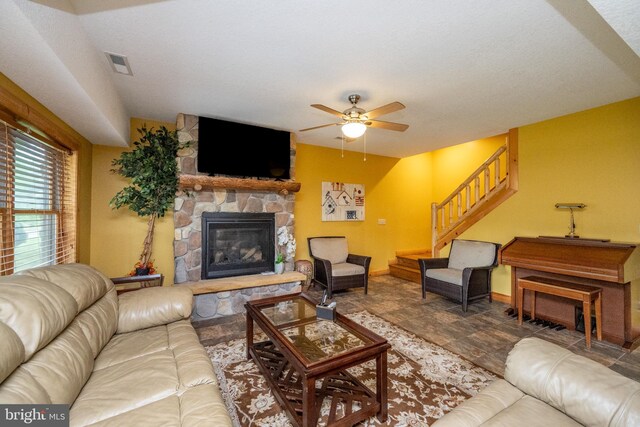 living room with a textured ceiling, ceiling fan, and a stone fireplace