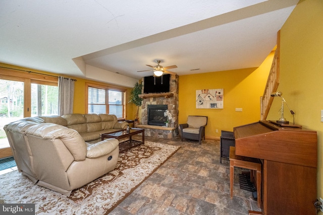 living area featuring ceiling fan, stone finish flooring, a fireplace, and baseboards