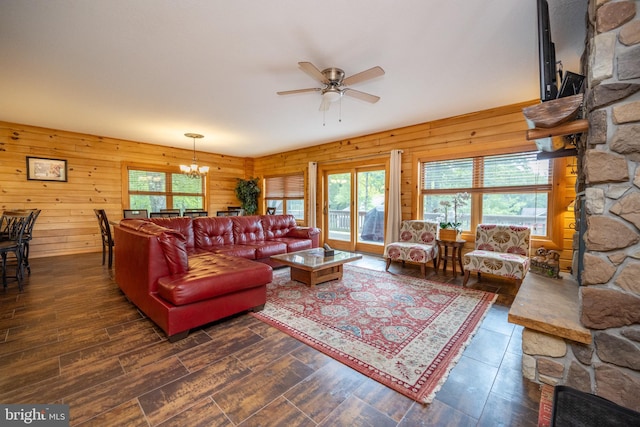 living room with ceiling fan with notable chandelier, wooden walls, and dark hardwood / wood-style flooring