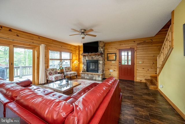 living room with dark wood-type flooring, a wealth of natural light, wooden walls, and a stone fireplace