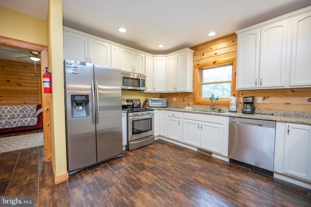 kitchen with appliances with stainless steel finishes, light stone countertops, white cabinetry, sink, and ceiling fan