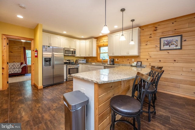 kitchen with hanging light fixtures, light stone counters, stainless steel appliances, kitchen peninsula, and dark wood-type flooring