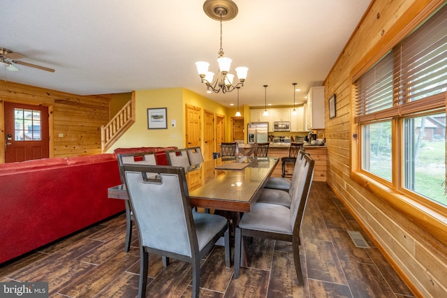 dining area featuring ceiling fan with notable chandelier, wood walls, and dark hardwood / wood-style floors