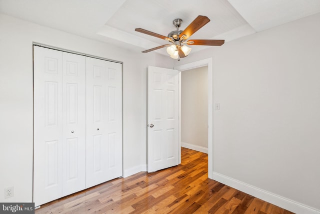 unfurnished bedroom with light wood-type flooring, a raised ceiling, ceiling fan, and a closet