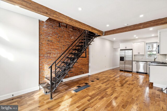 interior space with brick wall, appliances with stainless steel finishes, beam ceiling, and white cabinetry