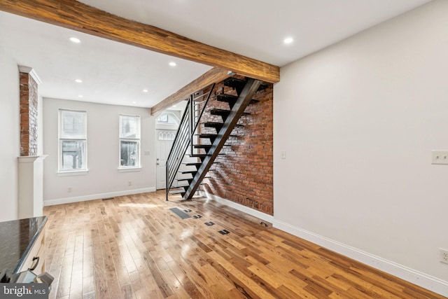 unfurnished living room with beam ceiling, hardwood / wood-style floors, and brick wall