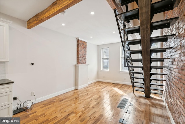 interior space featuring brick wall, beam ceiling, and light hardwood / wood-style floors