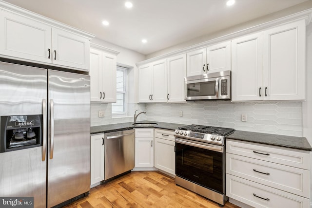 kitchen featuring dark stone counters, light hardwood / wood-style floors, sink, white cabinets, and appliances with stainless steel finishes