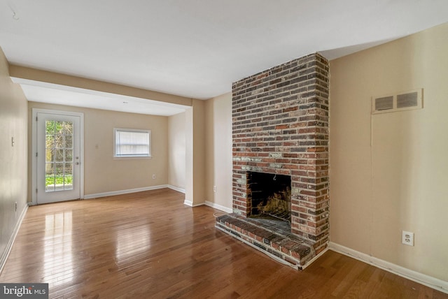 unfurnished living room with a brick fireplace, baseboards, visible vents, and wood finished floors