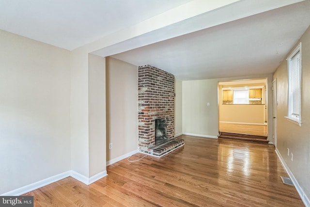 unfurnished living room with a brick fireplace, visible vents, baseboards, and wood finished floors