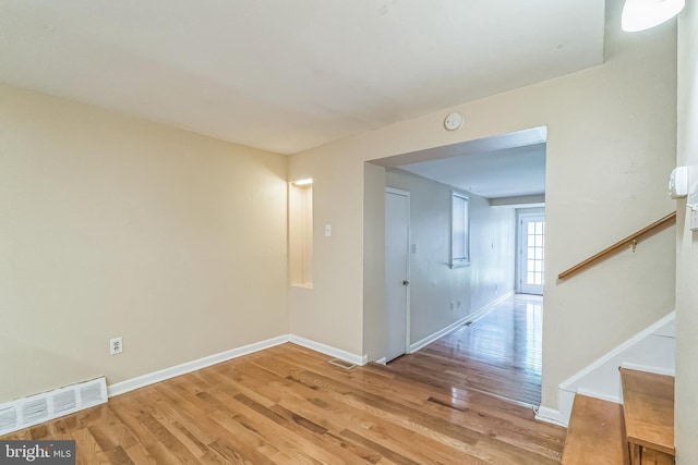 empty room featuring stairs, light wood finished floors, visible vents, and baseboards