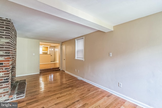 unfurnished living room featuring wood finished floors, beam ceiling, and baseboards