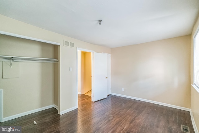 unfurnished bedroom with dark wood-style floors, a closet, visible vents, and baseboards