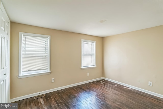 unfurnished room featuring dark wood-style floors, visible vents, and baseboards