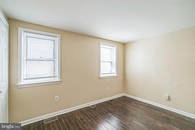 unfurnished room featuring dark wood-style floors, visible vents, and baseboards