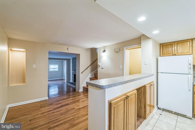 kitchen with baseboards, a peninsula, freestanding refrigerator, and light wood-style floors