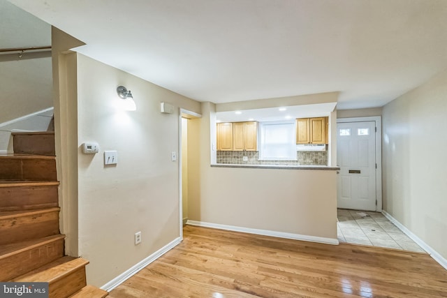 kitchen with light wood finished floors, tasteful backsplash, baseboards, light brown cabinetry, and under cabinet range hood