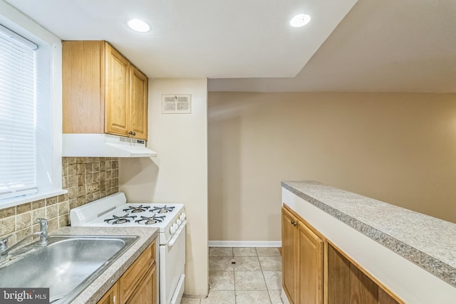 kitchen featuring gas range gas stove, light countertops, decorative backsplash, a sink, and under cabinet range hood