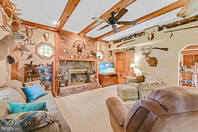 living room featuring a fireplace, beamed ceiling, ceiling fan, and carpet flooring