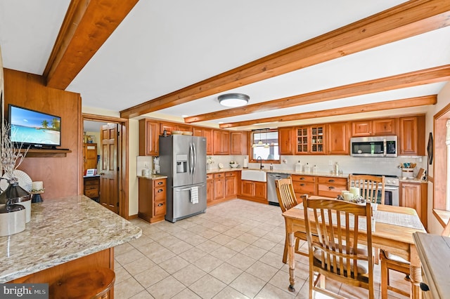 kitchen with light tile patterned floors, light stone counters, stainless steel appliances, beamed ceiling, and sink