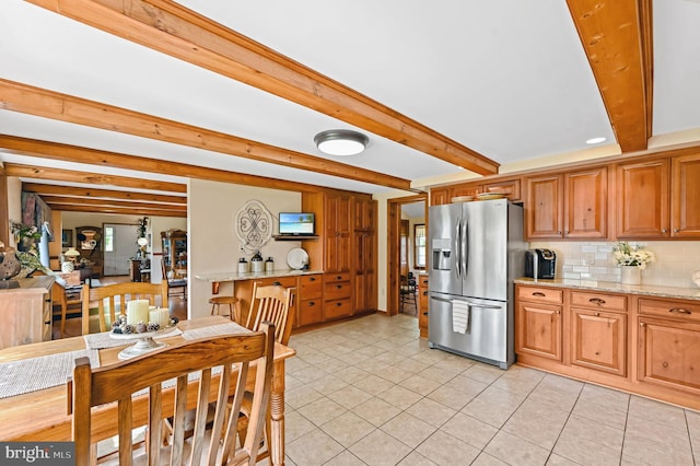 kitchen featuring light tile patterned floors, beam ceiling, stainless steel fridge with ice dispenser, decorative backsplash, and light stone counters