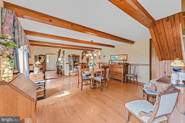 dining space featuring a textured ceiling, wood walls, beam ceiling, light hardwood / wood-style floors, and a chandelier