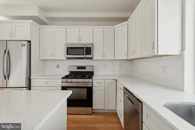 kitchen featuring white cabinets, light wood-type flooring, appliances with stainless steel finishes, light stone countertops, and tasteful backsplash