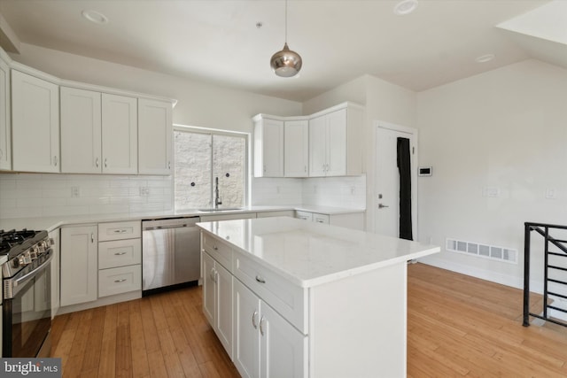 kitchen with a kitchen island, light hardwood / wood-style flooring, appliances with stainless steel finishes, tasteful backsplash, and hanging light fixtures