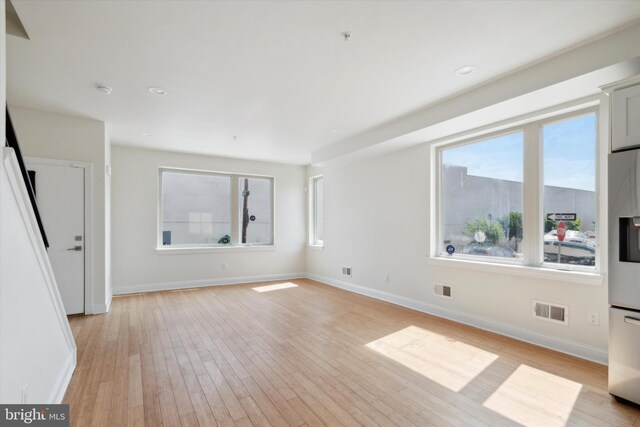 unfurnished bedroom featuring multiple windows, stainless steel fridge, and light hardwood / wood-style floors