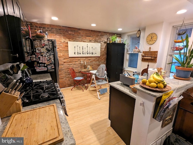 kitchen with black gas stove, light hardwood / wood-style floors, stainless steel refrigerator, and brick wall