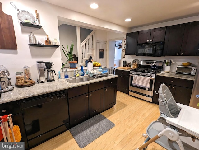 kitchen with black appliances, light stone counters, sink, and light hardwood / wood-style floors