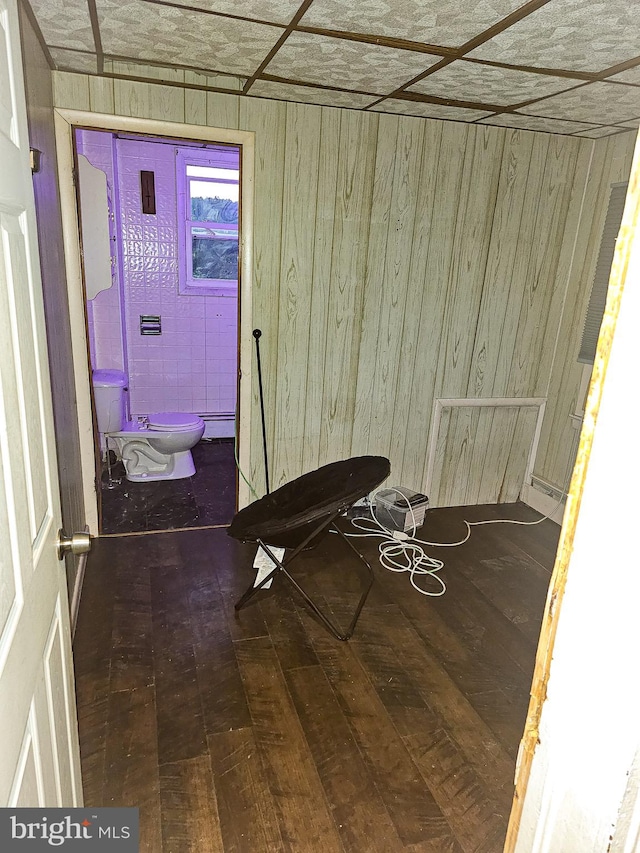 interior space featuring ensuite bathroom, a baseboard heating unit, wooden walls, and hardwood / wood-style floors